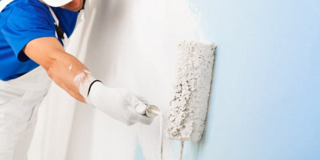 Professional painter in white uniform rolling light blue paint onto an interior wall