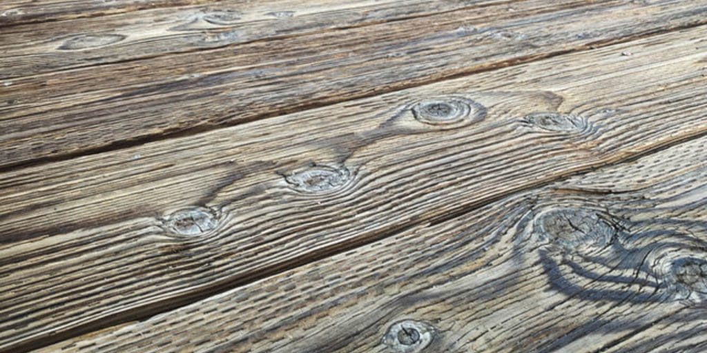 Close-up of weathered and graying wood deck boards showing surface roughness and grain breakdown from UV exposure and moisture damage